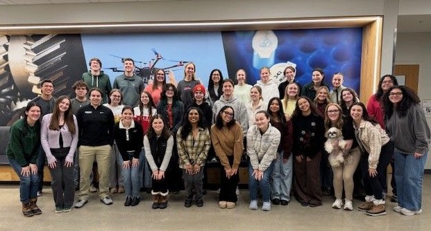 A large group in two lines of Exploratory Studies Student Ambassadors posing in front of wall. 